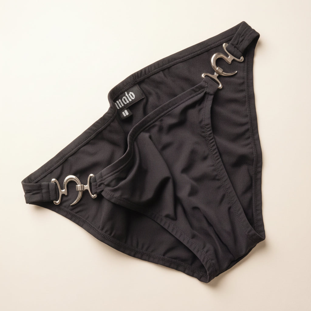 Black bikini bottoms featuring prominent silver horsebit hardware on the sides, laid flat on a light beige background. The brand name 'malo' is visible on a small black label near the waistband.