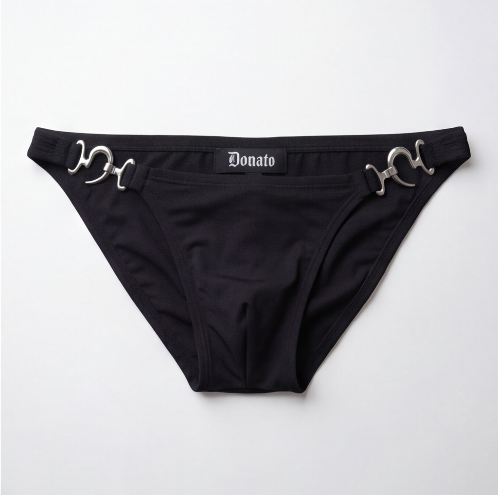 Black bikini bottom featuring silver horsebit hardware on the sides and a central black label with the white gothic-style 'Donato' brand name, laid flat on a light gray background.