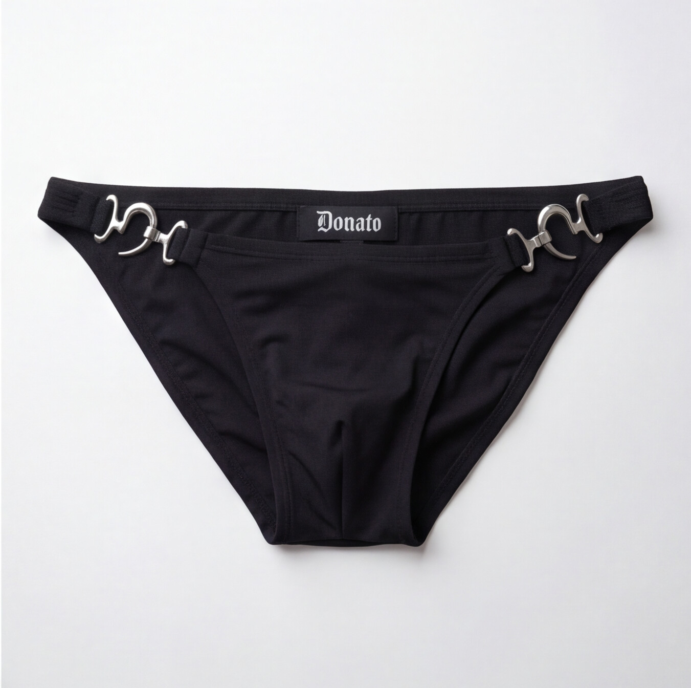 Black bikini bottom featuring silver horsebit hardware on the sides and a central black label with the white gothic-style 'Donato' brand name, laid flat on a light gray background.